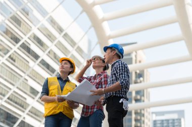 Asya mühendisleri grup planı kağıt basılı tutarak çalışma sitesi yapı inşaat bakın. Şehir arka planda. ekip çalışması kavramı