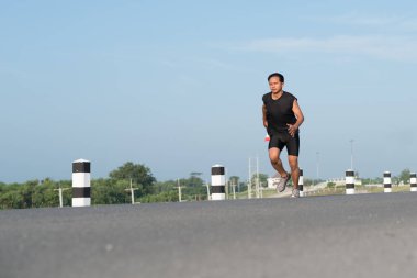 Asya genç adam gündoğumu dönemde baraj yolu egzersiz üzerinde çalıştırmak için. Sağlıklı yaşam tarzı