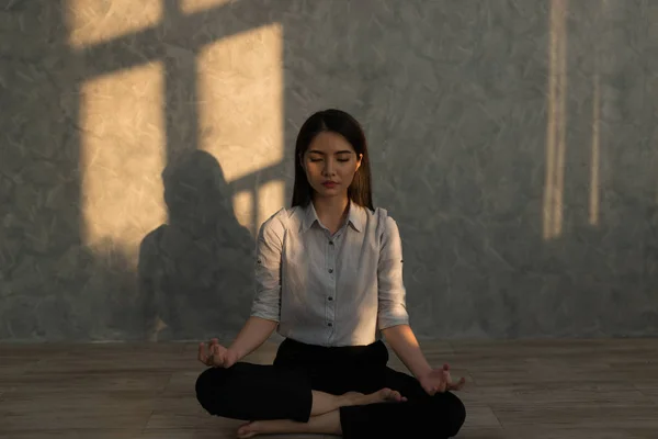 Beautiful asian young woman sitting in Lotos pose. Businesswoman practicing meditation in yoga hall after finish working. Time for Yoga and relaxation