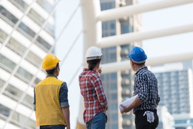 Asya mühendisleri grup planı kağıt basılı tutarak çalışma sitesi yapı inşaat bakın. Şehir arka planda. ekip çalışması kavramı