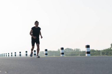 Asya genç adam gündoğumu dönemde baraj yolu egzersiz üzerinde çalıştırmak için. Sağlıklı yaşam tarzı