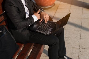 Tren istasyonunda oturan işadamı online bilgisayar dizüstü bilgisayarda çalışma saatine bakıyor. o zaman ve çalışmak için acele saatte acele görünüyor. Acele saat.