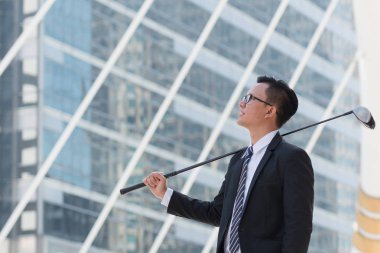 Takım elbiseli başarılı bir iş adamı. golf ekipmanları kentin ayakta tutan el. Şehir arka plan başarı kavramı