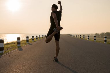 Asya genç germe egzersiz yaparak runner gündoğumu sırasında içinde verilen sürede baraj yolu egzersiz arka planda çalıştırmak için hazırlanıyor adam. Sağlıklı yaşam tarzı
