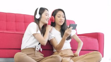 İki Asyalı genç kız yerde oturmuş evde kulaklıklarla müzik dinliyorlar. Kadın rahat, yaşam tarzı konsepti. 
