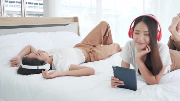 自宅のベッドで音楽を聞いて横にデジタルタブレットを使用してヘッドフォンで幸せな2人のアジアの10代の女の子 女性はリラックス ライフスタイル 若者と喜びの概念 ドリー スライダー ショット — ストック動画