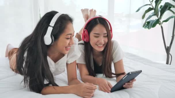 自宅のベッドで音楽を聞いて横にデジタルタブレットを使用してヘッドフォンで幸せな2人のアジアの10代の女の子 女性はリラックス ライフスタイル 若者と喜びの概念 — ストック動画