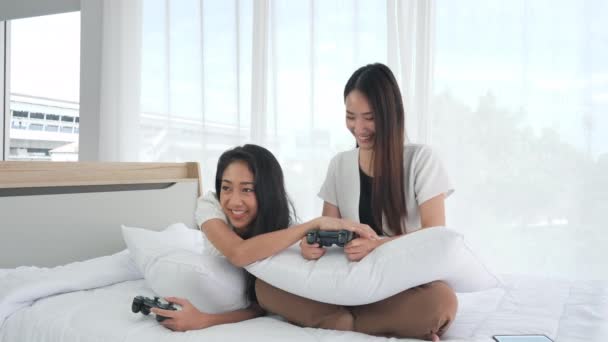 2人のアジアの10代の女の子が自宅でベッドの上でジョイスティックでビデオゲームを楽しんでいます 女性はリラックス ライフスタイル 若者と喜びの概念 — ストック動画