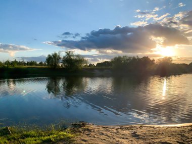 Doğal manzara, gün batımında nehir kıyısında. Manzara, sudaki yansıma, güneş ışınları, kıyıdaki çimenler. Akşamları nehir kenarında.