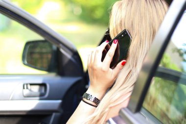 Arabada konuşan sarışın kız, kırmızı manikür, uzun saç, siyah telefon. Yakın plan, bulanık yeşil arka plan. Yaşam tarzı.