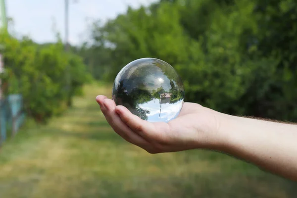Glass ball in a man's hand. reflection in glass. Blurred green background background, bokeh. Glossy, transparent ball.