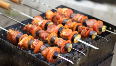 Dışarıdaki ızgarada şiş kebap, kömürde et, yakın plan. Duman, bulanık arka plan. Pelerin, domates, patlıcan, soğan.