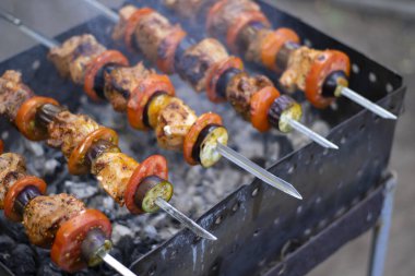 Dışarıdaki ızgarada şiş kebap, kömürde et, yakın plan. Duman, bulanık arka plan. Pelerin, domates, patlıcan, soğan.