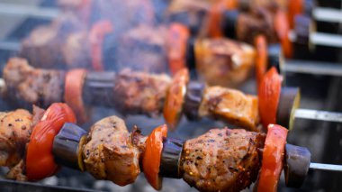Dışarıdaki ızgarada şiş kebap, kömürde et, yakın plan. Duman, bulanık arka plan. Pelerin, domates, patlıcan, soğan.