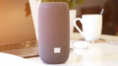 Dahili akıllı zekası olan taşınabilir bir konuşmacı. Müzikal köşe. Mermer masa, çalışma ortamı, laptop, yeşil çiçek, kahve fincanı. Sabah güneş ışığı.