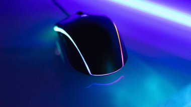 Beyaz parlak bir masa üzerinde neon ışıklı bilgisayar faresi, karanlık oda, neon ışık, diyotlar. Oyun aletleri, neon ışıklar, beyaz parlak masa. Yaşam tarzı, oyun alanı.