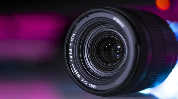 The camera lens is illuminated with neon light. Close-up. Dark neon background.