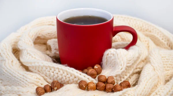Autumn background with a red cup of coffee, tea, on the window, knitted scarf. Autumn coffee, dry leaves. Season October, November. Close-up.