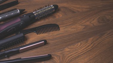 Ahşap bir arka planda kuaför aletleri. Taraklar, saç kurutma makinesi, saç düzleştirici. Uzun saç kıvırcıkları. Uzatılmış saç bakımı.