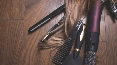 Ahşap bir arka planda kuaför aletleri. Taraklar, saç kurutma makinesi, saç düzleştirici. Uzun saç kıvırcıkları. Uzatılmış saç bakımı.
