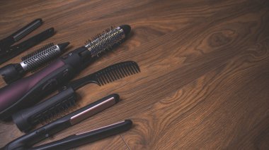 Ahşap bir arka planda kuaför aletleri. Taraklar, saç kurutma makinesi, saç düzleştirici. Uzun saç kıvırcıkları. Uzatılmış saç bakımı.