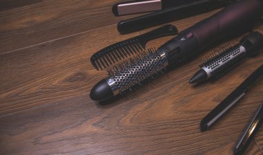 Ahşap bir arka planda kuaför aletleri. Taraklar, saç kurutma makinesi, saç düzleştirici. Uzun saç kıvırcıkları. Uzatılmış saç bakımı.