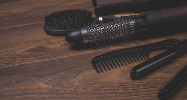 Ahşap bir arka planda kuaför aletleri. Taraklar, saç kurutma makinesi, saç düzleştirici. Uzun saç kıvırcıkları. Uzatılmış saç bakımı.