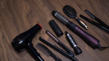 Ahşap bir arka planda kuaför aletleri. Taraklar, saç kurutma makinesi, saç düzleştirici. Uzun saç kıvırcıkları. Uzatılmış saç bakımı.