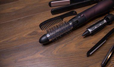 Ahşap bir arka planda kuaför aletleri. Taraklar, saç kurutma makinesi, saç düzleştirici. Uzun saç kıvırcıkları. Uzatılmış saç bakımı.