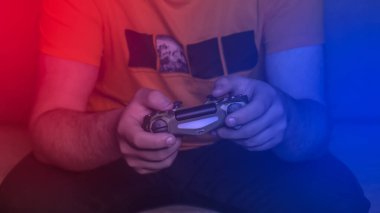 Oyun kumandalı erkek eller, oyun alanı. Genç adam konsolda oynuyor. Kırmızı mavi neon ışık. Evde video oyunu oynayan erkek ellerini kapat..