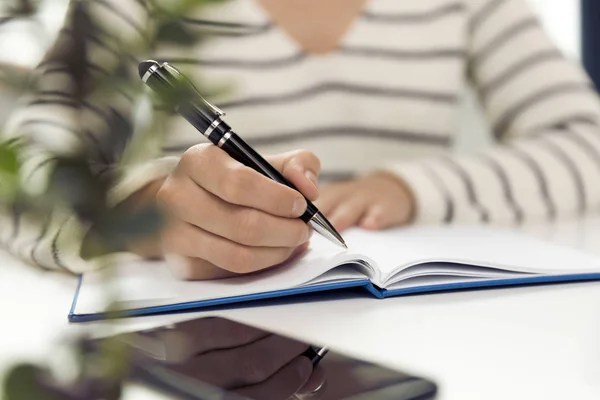 Joven Mujer Negocios Sentada Mesa Escribiendo Cuaderno Mesa Está Smartphone —  Fotos de Stock