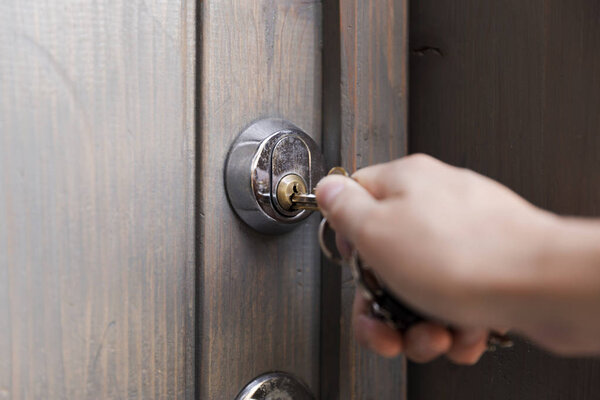 Женская рука кладет ключ в замочную скважину деревянной двери. Концепция безопасности

