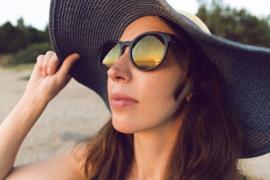 Genç ve güzel kadın günbatımı ışık uzakta ufka bakarak bir şapka