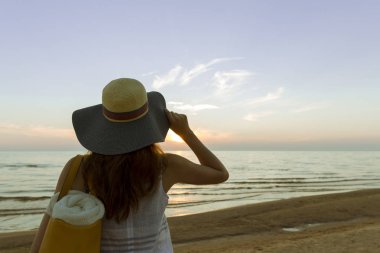 Genç ve güzel kadın günbatımı ışık uzakta ufka bakarak bir şapka