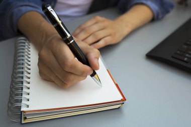 Defterine kalem yazan kadın elleri. Modern gri ofis masası. Çalışma, yazma kavramı