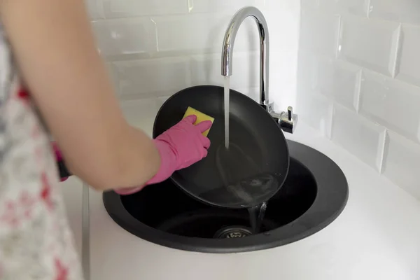 Female hand washing frying pan under running water. Young housewife woman washing griddle in a kitchen sink with a yellow sponge, Hand cleaning, manually, by hand, housework dishwasher