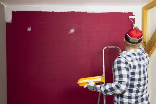 Home improvement. A man in a red hat coloring a room with a paint roller and paint brush.