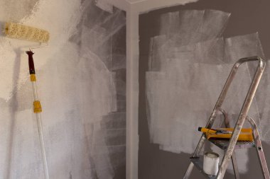 Boyama aletleri, boya silindiri, fırça, alüminyum lider. Duvar kısmen renklendirilmiş.