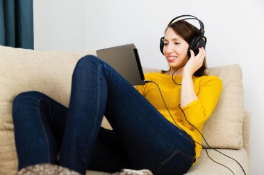 Güzel kadın kanepe oturma ve kulaklık ile dinleme. E-öğrenme kavramı.