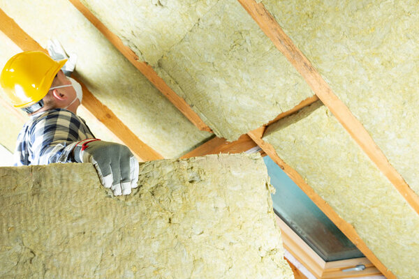 Man installing thermal roof insulation layer - using mineral wool panels. Attic renovation and insulation concept