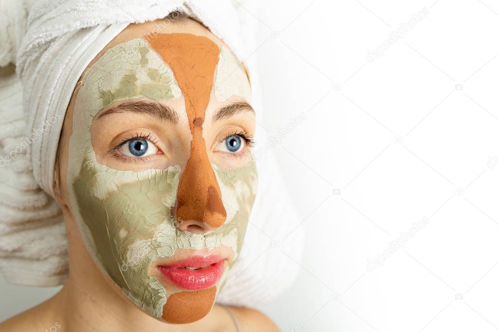 Beauty procedures skin care concept. Young woman applying facial gray and red mud clay mask to her face in bathroom. Woman with different masks on her face multi-masking