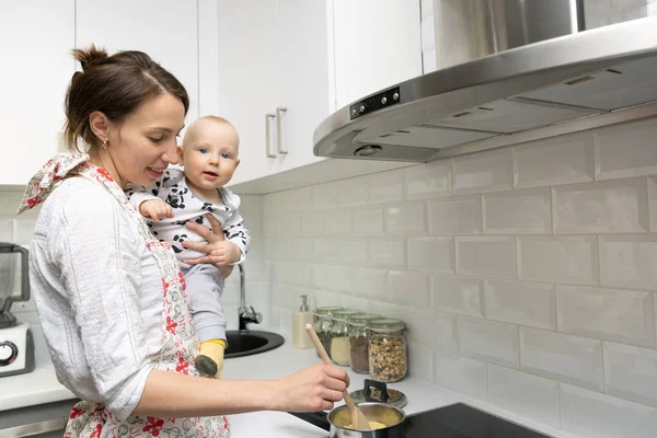 Elleri üzerinde bir bebekle genç anne aşçılar bir tencerede gıda üzerinde