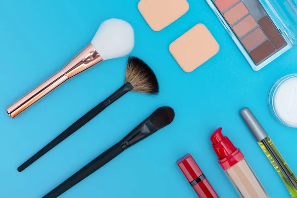 Cosmétiques décoratifs, produits de maquillage et brosses sur fond bleu — Photo