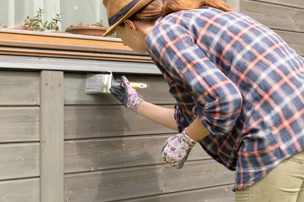 Женщина-работница красит наружную стену деревянного дома кистью — стоковое фото