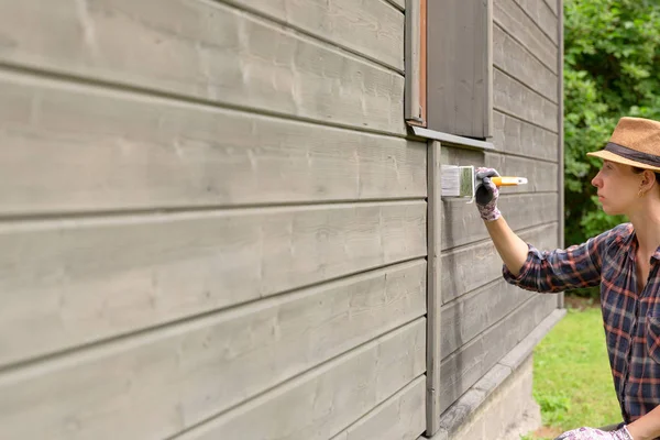 Woman worker painting wooden house exterior wall with paintbrush