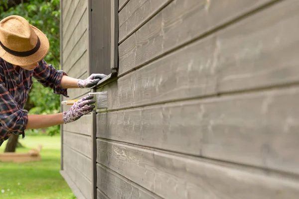 Woman worker painting wooden house exterior wall with paintbrush