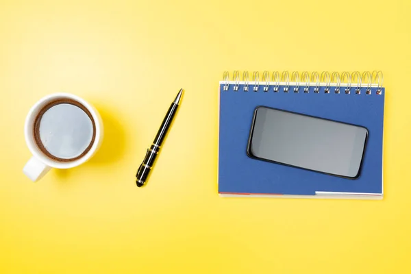 Notebook, smartphone, mobil, kaffe och penna på en gul backgro — Stockfoto