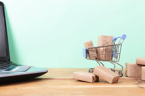 Online shopping concept. Shopping cart, small boxes, laptop and — Stock Photo, Image