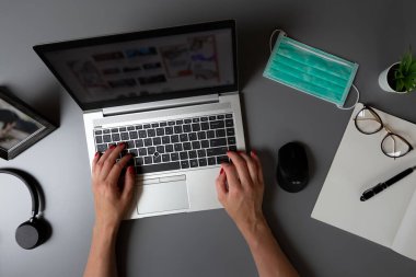 Merkez ofisin en iyi manzarası. Yüz koruma maskesiyle gri bir masada dizüstü bilgisayarda yazı yazan kadınların elleri..