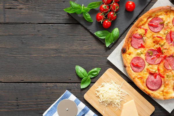 Tasty hot pizza with ingredients and pizza cutting knife on a black texture background Top view